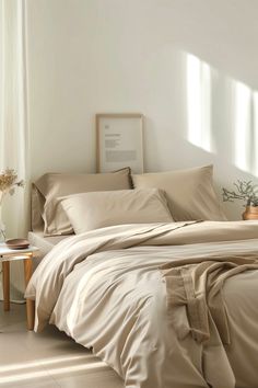 a bed with beige sheets and pillows in a white room next to a window on the floor