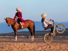 two people riding on the backs of brown horses in desert area with mountains in background