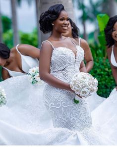 two beautiful women in white dresses standing next to each other and one is holding a bouquet