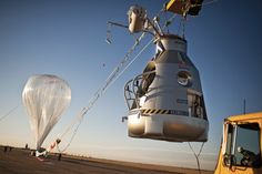 two hot air balloons are being lifted from the ground by a crane while another balloon floats in the sky