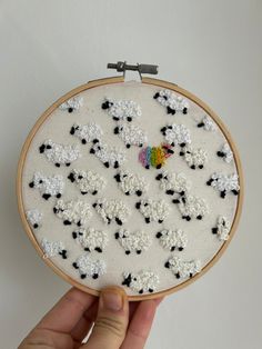 a hand is holding up a small embroidery project with sheep and rainbow in the middle