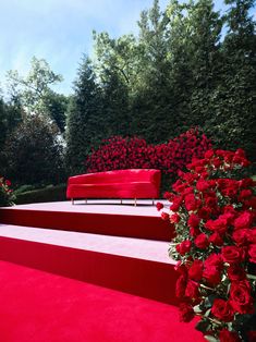 a red couch sitting on top of a set of steps next to flowers and trees