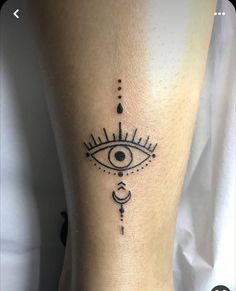 an eye tattoo on the ankle is shown in black and grey ink, with symbols around it