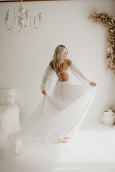 a woman in a white dress standing on a bed with her back to the camera