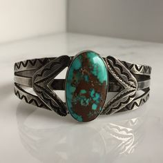 "Details: Lovely Native American Sand Cast Turquoise and Silver Bracelet. The turquoise is a deep blue with silver veins, and measures 1\" x 3/4\", and the face of the bracelet measures 1 3/4\" high. This piece has a nice weight to it. Please ask all necessary questions prior to placing an order. Measurements: The bracelet is a cuff, and can be adjusted to fit small to medium wrists. The interior measures 2 1/2 across, and the interior measures 5 1/2 inches.. Condition: The overall all condition Classic Turquoise Adjustable Bracelet, Turquoise Cuff Bracelet With Polished Finish, Southwestern Engraved Blue Cuff Bracelet, Adjustable Turquoise Cuff Bracelet With Polished Finish, Classic Turquoise Cuff Bracelet Gift, Adjustable Turquoise Polished Cuff Bracelet, Classic Adjustable Turquoise Cuff Bracelet, Floral Bracelet, Turquoise Bracelet Cuff