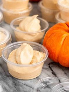 several small plastic cups filled with food on top of a marble table next to an orange pumpkin