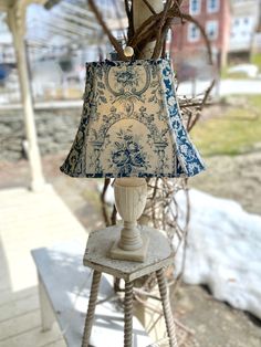 a table lamp sitting on top of a wooden stool next to a tree branch and building