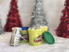 two plastic cups with lids are sitting in the snow next to christmas trees and money