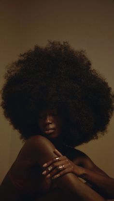 a woman with an afro is sitting on the floor and has her arms folded out