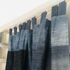 several blue and black curtains hanging from a wooden rod in front of bookshelves