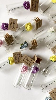 small glass bottles with flowers in them on a white surface, labeled with name tags