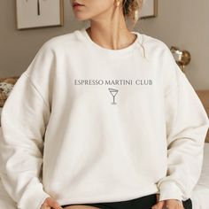 Wrap yourself in cozy comfort with our Espresso Martini Club sweater. Simple yet stylish, this sweater is perfect for casual outings or lounging at home. Whether you're a coffee lover or a cocktail enthusiast, this sweater is sure to become a favourite. Available in a range of sizes, treat yourself or surprise a friend with this delightful piece of wearable art Unisex Gildan 1800 heavy blend crewneck sweatshirt is pure comfort. These garments are made from 50% polyester and 50% cotton. This comb White Winter Tops For Lounging, White Winter Sweatshirt For Lounging, Cozy White Sweatshirt For Lounging, Graphic Print Crew Neck Top For Lounging, Casual Tops With Letter Print For Lounging, Martini Please, Coffee Sweater, Espresso Martini, Comforters Cozy