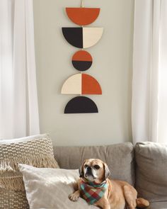 a brown dog laying on top of a couch in front of a wall hanging with geometric shapes