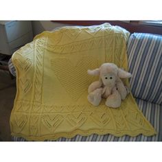 a teddy bear sitting on top of a yellow crocheted blanket next to a blue and white striped pillow