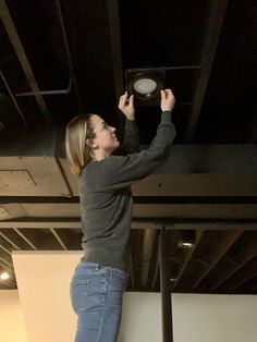 a woman standing on top of a metal pole while holding onto a ceiling light fixture