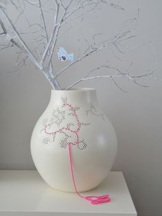 a white vase sitting on top of a table next to a tree with branches in it