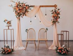 the wedding arch is decorated with peach flowers and greenery, along with two wooden chairs