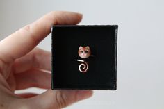 a person holding up a tiny ring with a cat on it's face in a black box