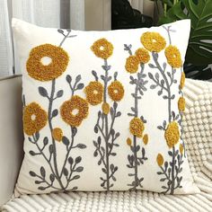 a pillow with yellow flowers on it sitting on a white couch next to a potted plant