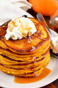 a stack of pancakes on a plate with whipped cream and oranges in the background