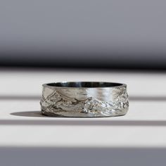 a silver ring with mountains on it sitting on top of a white table next to a window