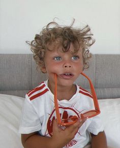 a little boy sitting on top of a bed holding a pair of scissors in his mouth