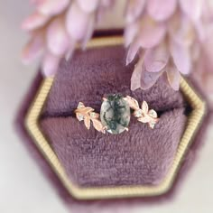 an engagement ring sitting on top of a purple velvet box with flowers in the background