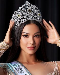 a beautiful young lady wearing a tiara and holding her hair in the air with both hands