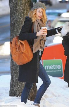 a woman holding a coffee cup and wearing a brown bag while standing next to a tree