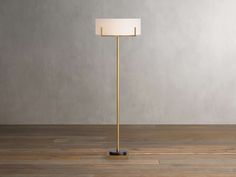 a floor lamp with a white shade on the top and a black base, in front of a gray wall