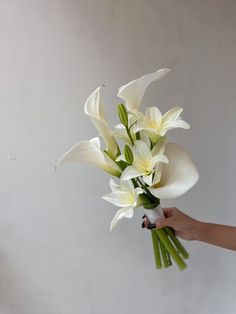 a bouquet of white flowers being held by a woman's hand in front of a wall