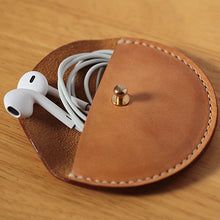 an apple earbud in a leather case on a wooden table with the cord plugged into it