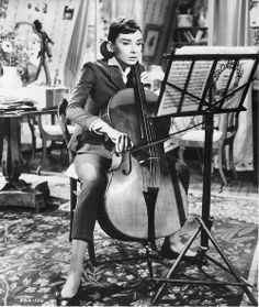 a woman is playing the cello in an old black and white photo with music instruments behind her