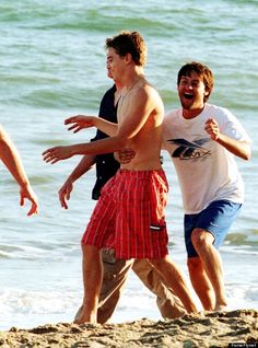 three men are playing frisbee on the beach while another man watches from the shore