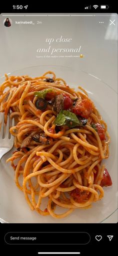 a white plate topped with pasta covered in sauce and vegetables next to a fork on top of a table