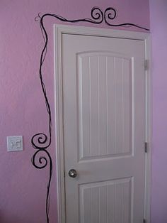 a white door in a pink room with a black vine design on the wall next to it