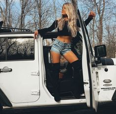 a woman standing in the open door of a white jeep with her legs crossed and wearing black boots