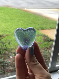 a hand holding a heart shaped object in front of a window