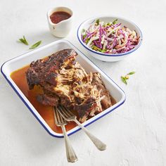 a plate with meat and coleslaw next to a bowl of coleslaw