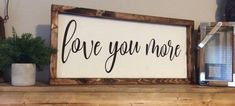 a wooden sign that says love you more next to a potted plant on a mantle