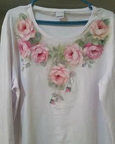 a white shirt with pink flowers on it is hanging from a hanger in front of a wall