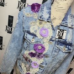 a blue jean jacket with purple flowers and lace on the back, sitting on top of a mannequin's head