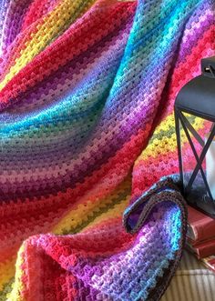 a multicolored crocheted blanket next to a lantern