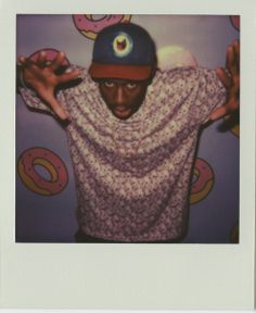 a man wearing a hat and sweater with doughnuts on the wall behind him