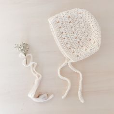 a crocheted white bonnet next to a flower on a wooden table with a string