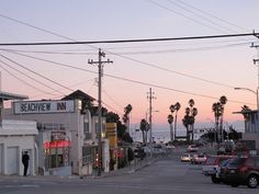 a street with cars parked on both sides and palm trees in the background at sunset