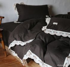 an unmade bed with black and white comforter on it's side, next to a wooden chair