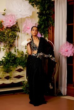 Black is your new summer romantics to go all glam for any intimate soiree of the season. This pre-draped saree highlighted with the lines of black bead-work all around comes with a dazzling floral blouse accentuated with embroidered multicolor bead-work and cut-work. The floral bead embroidery also highlights the waistline and goes on the pallu’s borders. Sleeveless blouse with a deep neck and cutwork detailing at the edges. Hook at the back of the blouse. The silk satin pre-draped saree is acce Draped Saree, Butterfly Net, Drape Saree, Black Saree, Organza Saree, 12 Weeks, Bead Embroidery, Cut Work, Floral Blouse