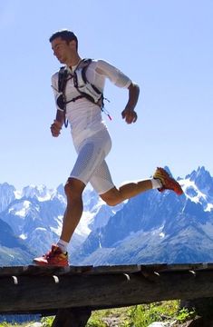 a man running across a wooden bridge with mountains in the background