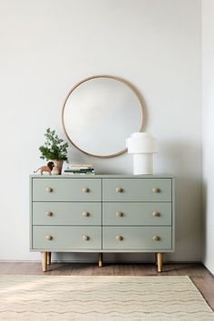 a green dresser with a round mirror above it and a plant in front of it